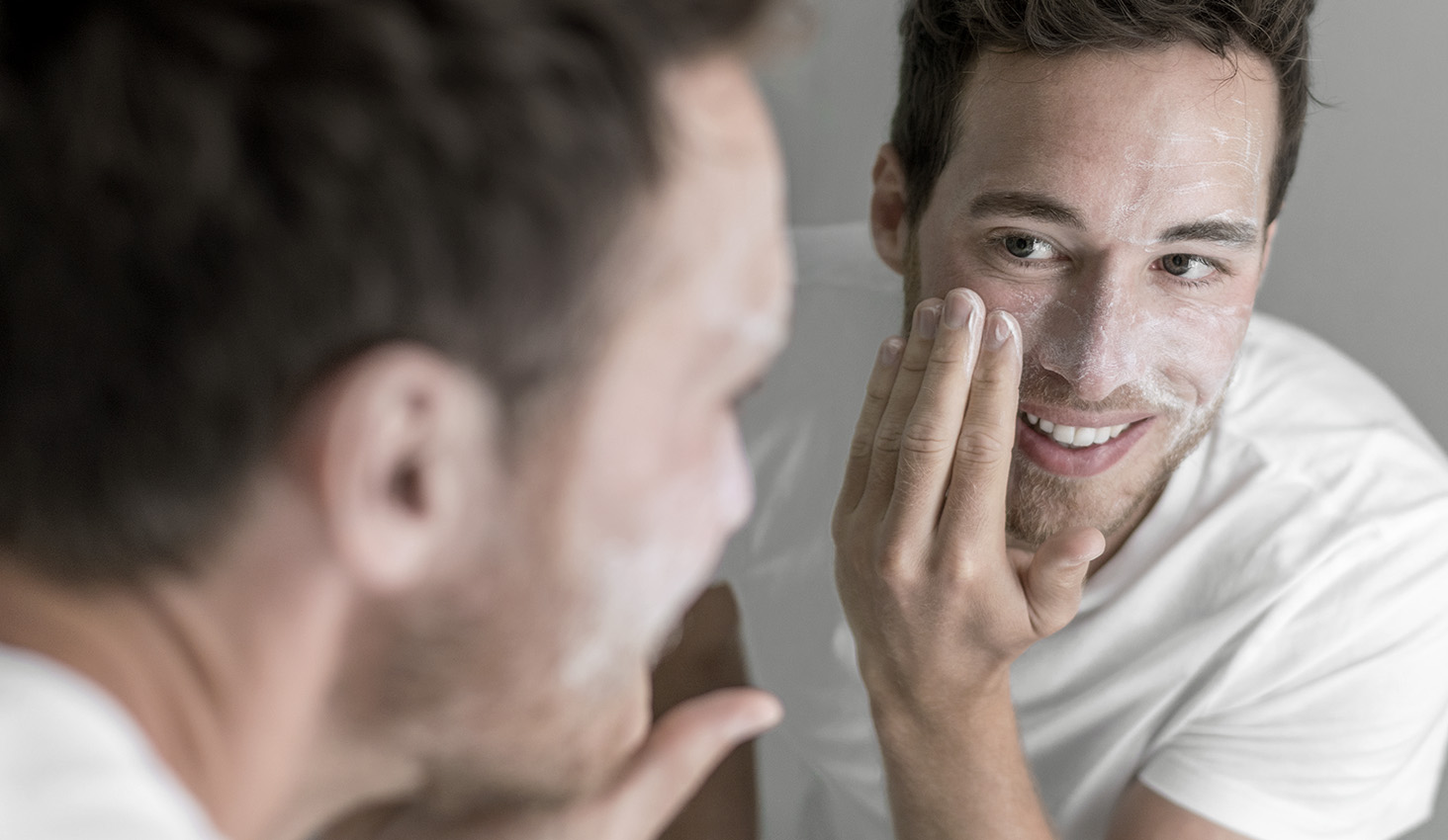 Hombre aplicándose crema en el rostro frente al espejo para hidratar la piel