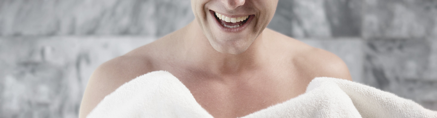 Hombre en la ducha sosteniendo una toalla después del baño, reflejando una rutina de cuidado de la piel